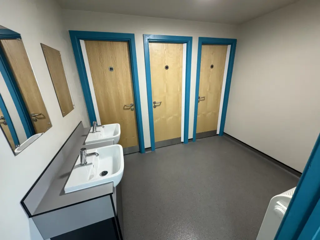 Completed washroom at The Hawthorns School in Chelmsford with teal-framed cubicles and a low-level vanity unit