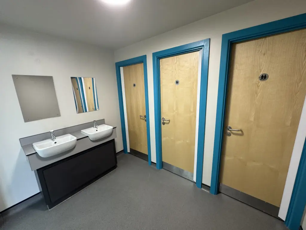 Wide completed view of The Hawthorns School washroom in Chelmsford showing the cubicles, vanity and accessible WC door
