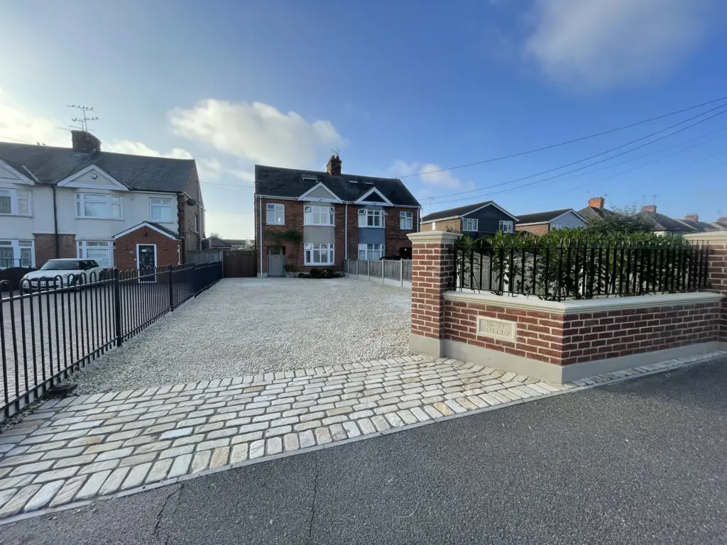 Finished brick and ironwork driveway entrance with sandstone cobble apron in Witham