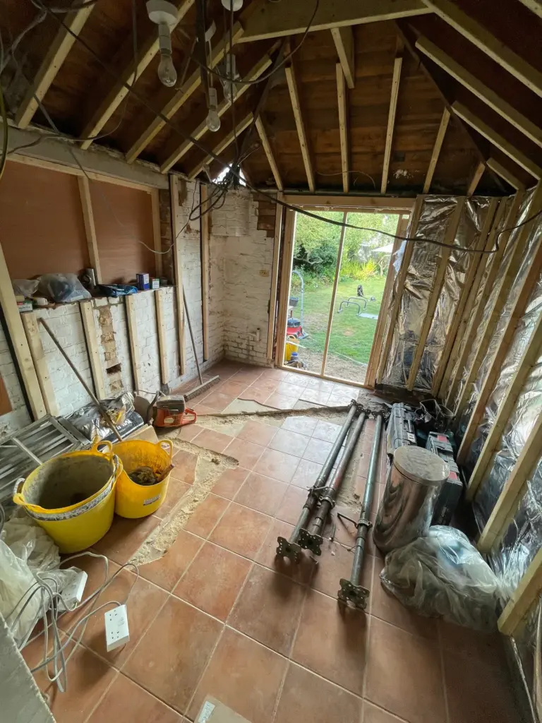 New timber stud frame and roof insulation during the Witham outbuilding conversion, with a new window opening formed in the brick wall