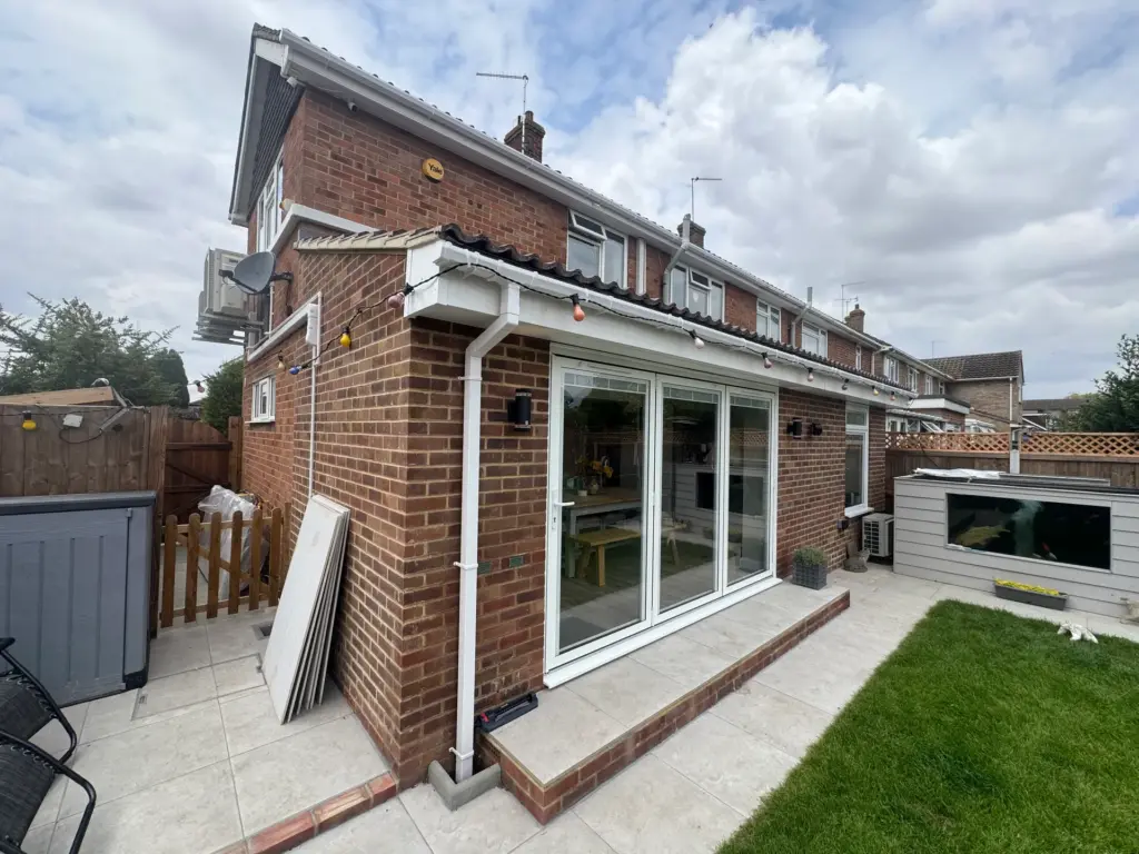 Corner of the brick-built rear extension in Writtle with matched brickwork, white aluminium bi-fold doors and porcelain patio